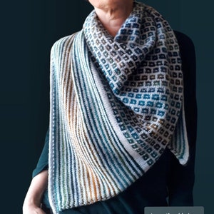 May include: A triangular shawl with a geometric pattern in shades of blue, green, brown, and white. The shawl is knit with a striped pattern on one side and a square pattern on the other side.