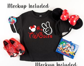 May include: Black t-shirt with red and white text that says "Oh, Twodles" with a Mickey Mouse head and hand with two fingers up. The shirt is on a white surface with red shoes, a Mickey Mouse headband, and a Disney autograph book.