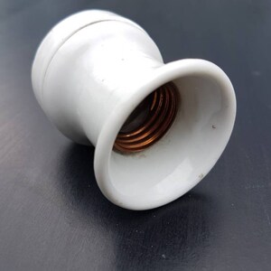 May include: White ceramic light bulb socket with a copper threaded center.