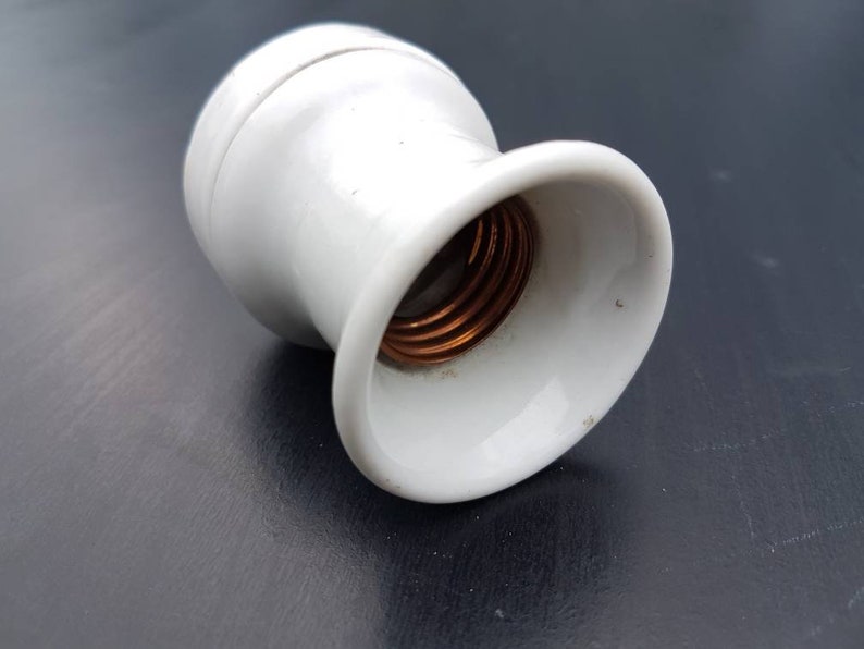 May include: White ceramic light bulb socket with a copper threaded center.