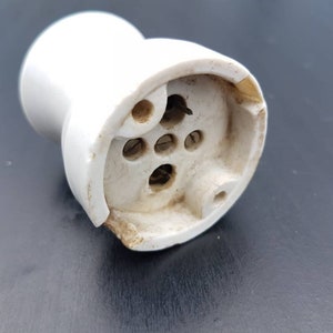 May include: White ceramic electrical outlet with four holes for wiring. The outlet is designed for use with a light bulb.