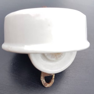 Peut inclure: Poulie en porcelaine blanche avec un crochet en métal. La poulie a une surface lisse et arrondie et un petit trou au centre.