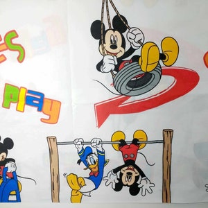 K&ouml;nnte beinhalten: Ein wei&szlig;er Stoff mit einem bunten Druck, der Mickey Mouse und Donald Duck zeigt. Der Druck enth&auml;lt die W&ouml;rter "Smiles Play" und "Smile".