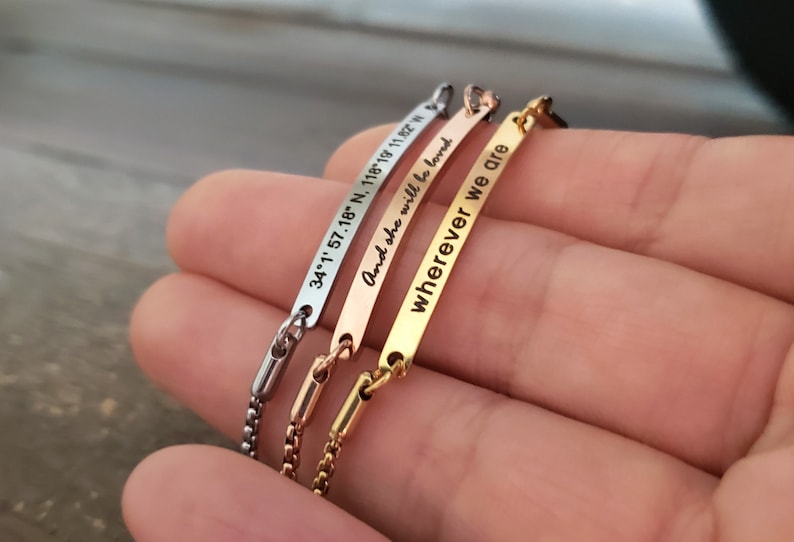 K&ouml;nnte beinhalten: Drei Armb&auml;nder aus Silber, Gold und Ros&eacute;gold mit graviertem Text. Das silberne Armband tr&auml;gt die Aufschrift "34.1' 57.18' N, 118.19' 11.92' W". Das goldene Armband tr&auml;gt die Aufschrift "And she will be loved". Das ros&eacute;goldene Armband tr&auml;gt die Aufschrift "wherever we are".