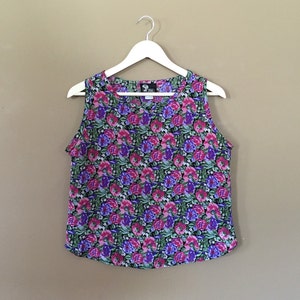 May include: A sleeveless floral print top with a scoop neck. The top is a mix of pink, purple, green, and white flowers on a black background.