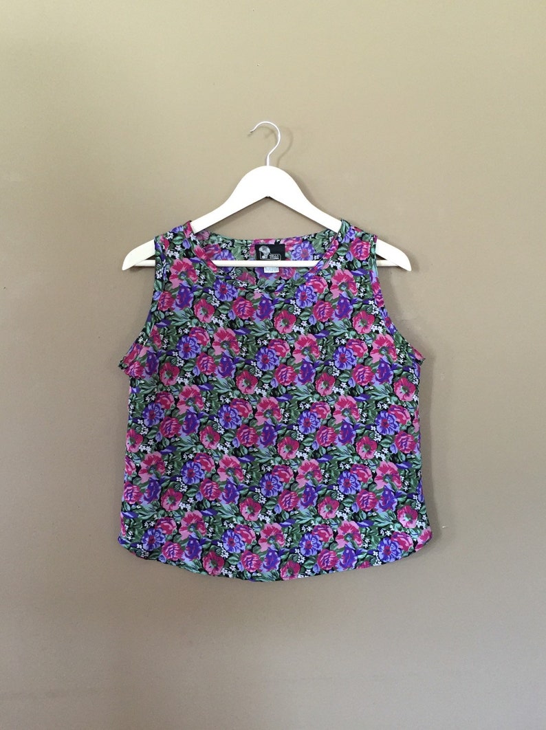 May include: A sleeveless floral print top with a scoop neck. The top is a mix of pink, purple, green, and white flowers on a black background.