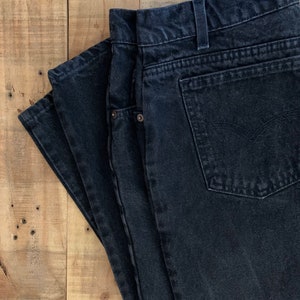 May include: A pair of black denim jeans folded on a wooden surface.