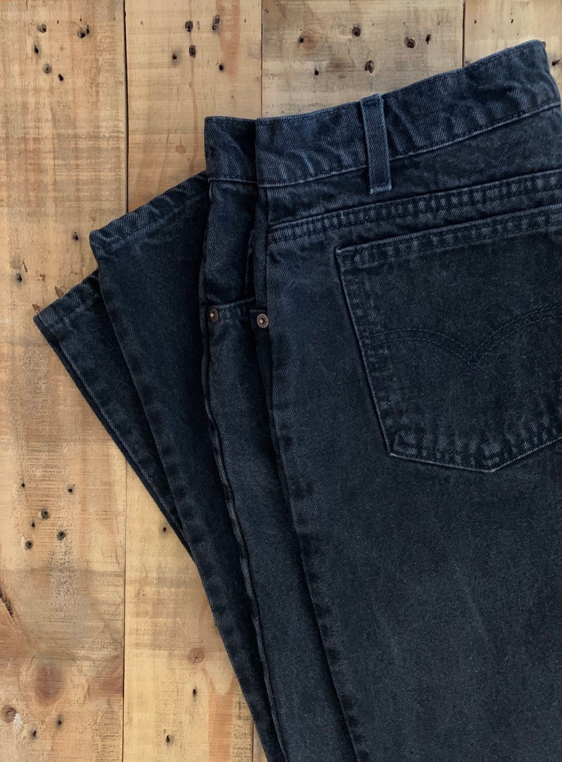 May include: A pair of black denim jeans folded on a wooden surface.