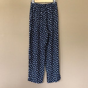 Puede incluir: Pantal&oacute;n negro con estampado floral blanco. El pantal&oacute;n est&aacute; colgado en una percha de madera.