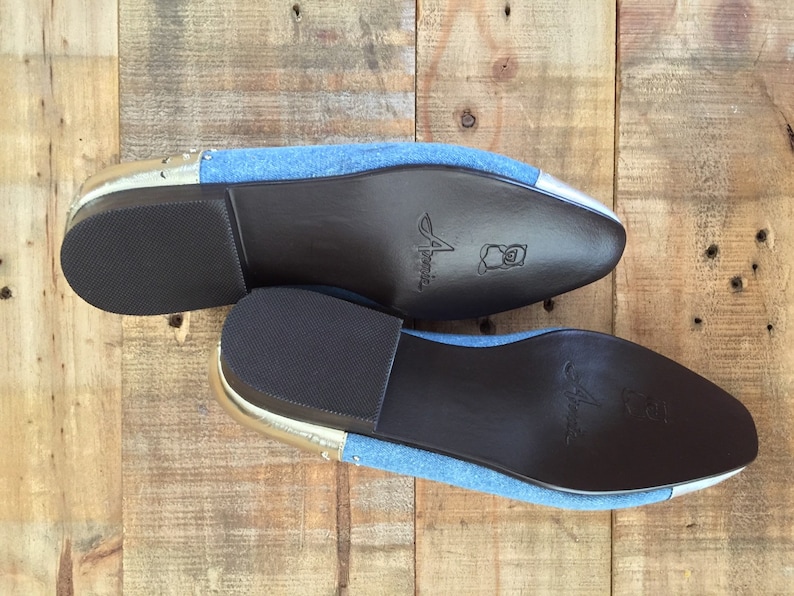 Puede incluir: Un par de zapatos de mezclilla azul con ribetes plateados y suelas de cuero marr&oacute;n. Las suelas est&aacute;n marcadas con la palabra "Amelia".