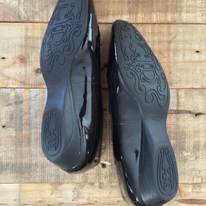 May include: A pair of black patent leather shoes with a decorative design on the soles. The shoes have a pointed toe and a low heel.