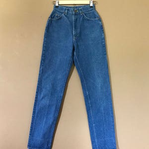 May include: A pair of blue denim jeans hanging on a wooden hanger against a brown background.