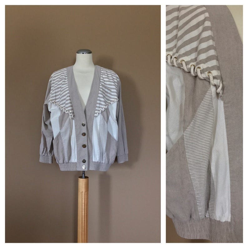 May include: A beige cardigan with white stripes and a V-neck. The cardigan has a button closure and a ribbed hem.