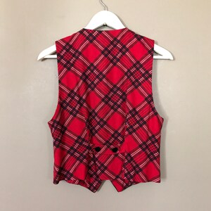 May include: A red and black plaid vest with a pointed collar and a button closure. The vest is sleeveless and has a slightly fitted silhouette.