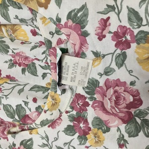 K&ouml;nnte beinhalten: Wei&szlig;er Stoff mit einem Blumendruck mit rosa und gelben Blumen. Der Stoff hat ein Etikett mit der Aufschrift "50% Polyester 50% Algodon Made in U.S.A. Hecho en E.U.A.  Cuta 12-109 Style 079622 Size Large/Grande"
