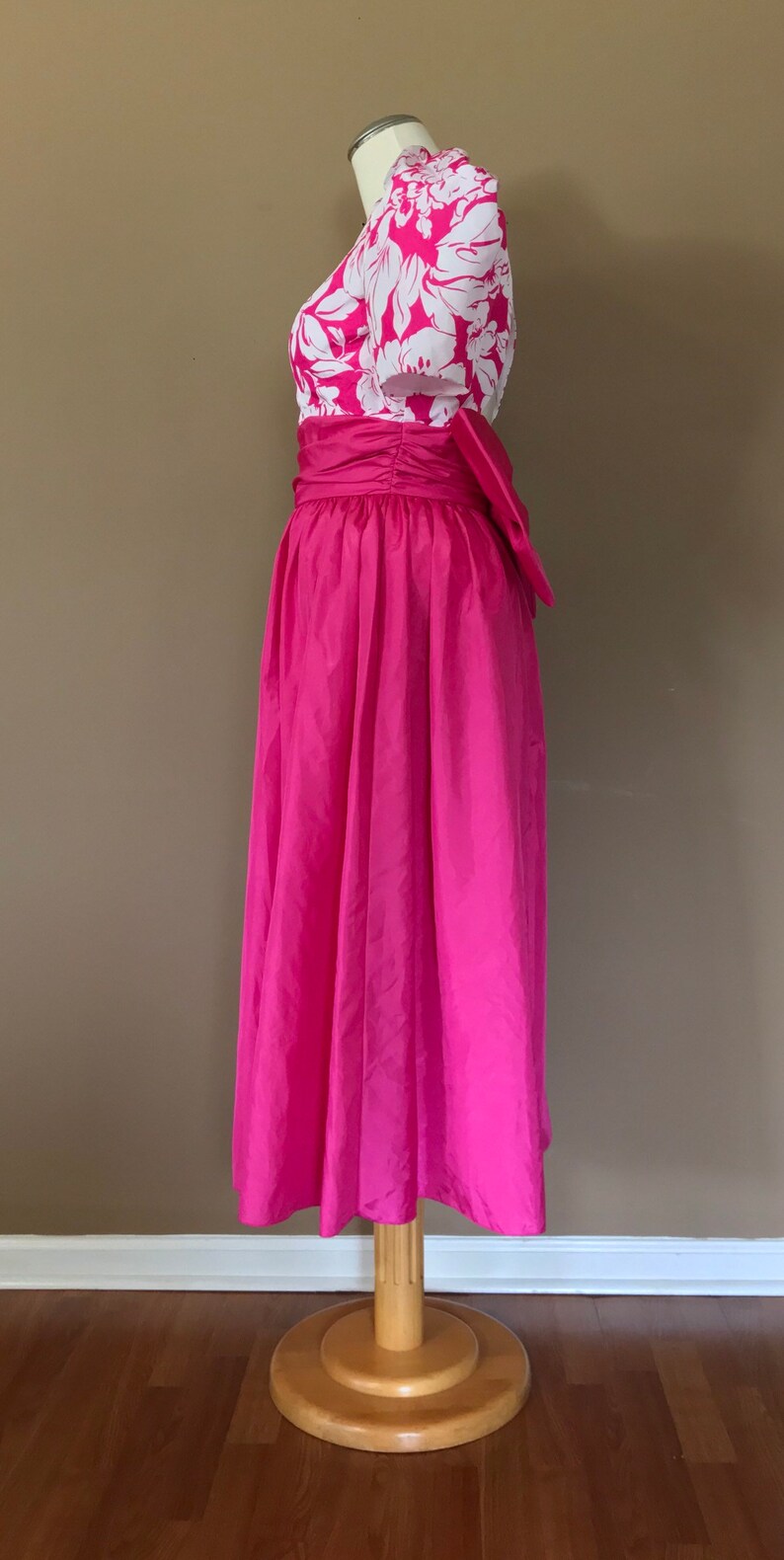 Puede incluir: Un vestido rosa con un corpi&ntilde;o de estampado floral blanco y una falda completa. El vestido tiene una faja que se ata en un lazo en la espalda.