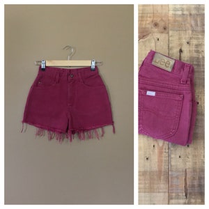 May include: High-waisted denim shorts in a deep burgundy color with frayed edges. The shorts have a classic five-pocket design and a Lee logo patch on the back.