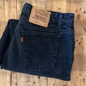 May include: Black denim jeans with a Levi Strauss & Co. label. The label is brown with white text and features a horse and rider logo. The jeans are folded in half and the label is visible on the back pocket.