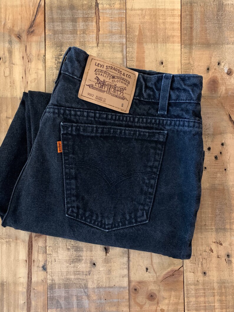 May include: Black denim jeans with a Levi Strauss & Co. label. The label is brown with white text and features a horse and rider logo. The jeans are folded in half and the label is visible on the back pocket.