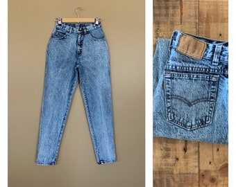May include: Light blue high-waisted jeans with a faded wash and a button fly. The jeans have a relaxed fit and are made of a soft denim fabric.
