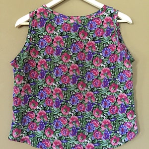 May include: A sleeveless top with a floral print featuring pink, purple, and green flowers on a black background.