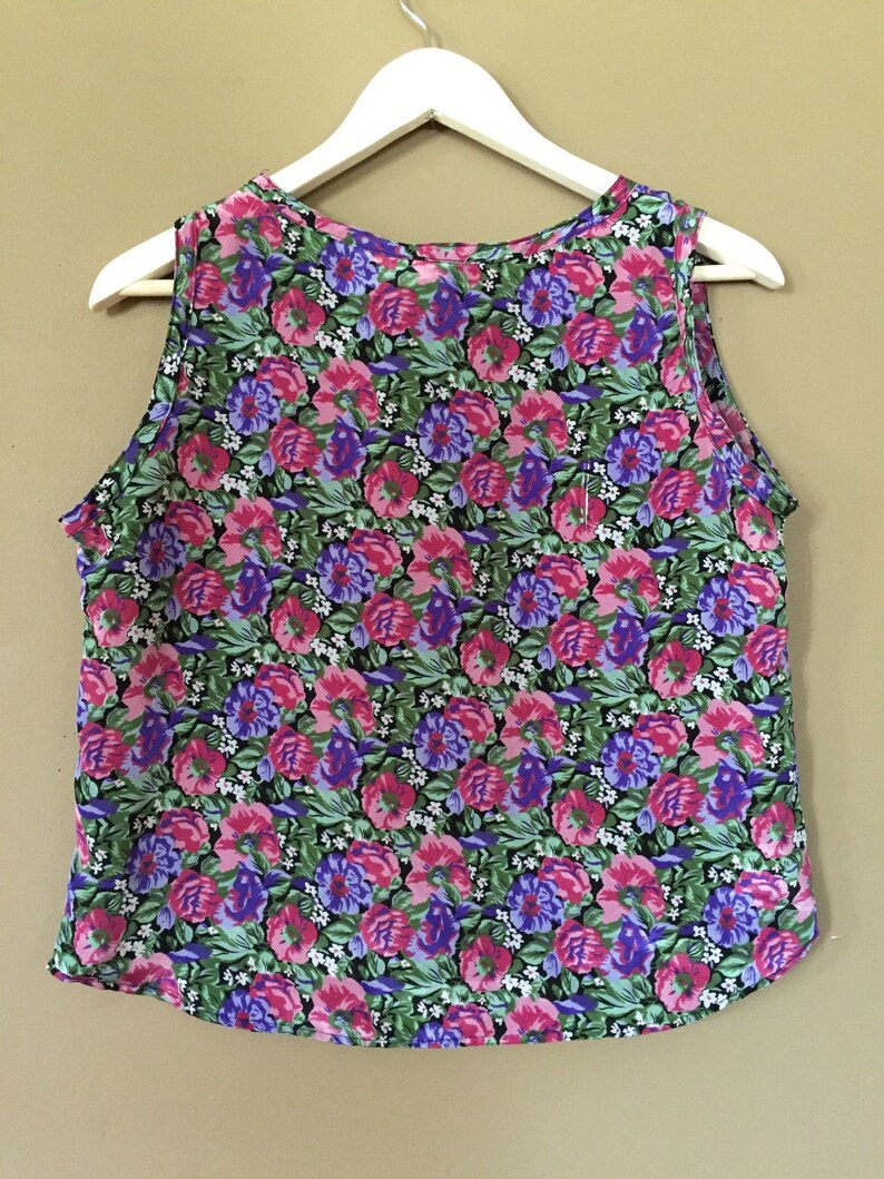 May include: A sleeveless top with a floral print featuring pink, purple, and green flowers on a black background.