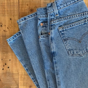 May include: A stack of three pairs of light blue denim jeans folded on a wooden surface.