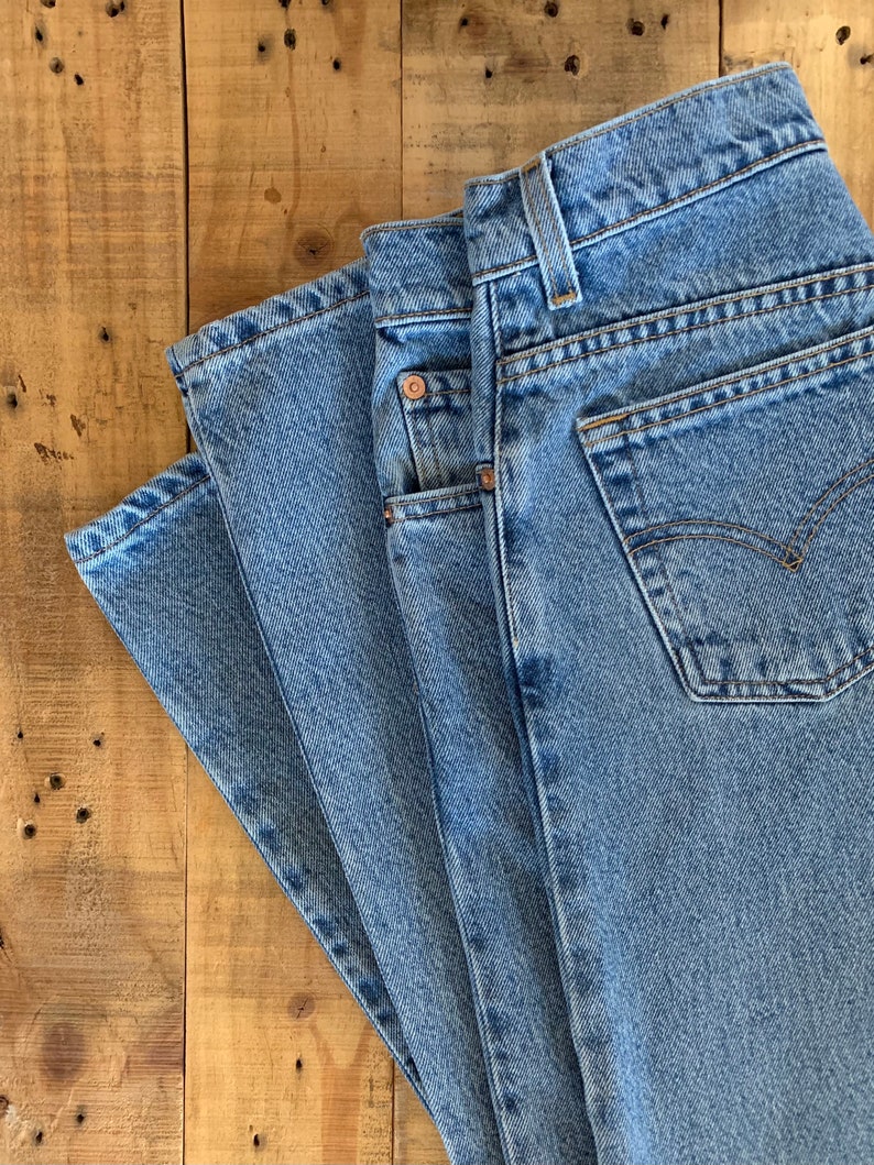 May include: A stack of three pairs of light blue denim jeans folded on a wooden surface.