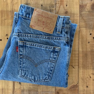 May include: A pair of blue denim jeans with a brown leather Levi Strauss & Co. patch on the back pocket. The patch has the text "Original Quality Clothing" and "Every Garment Guaranteed" with the size 555 and W LM.