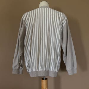 May include: A beige striped long-sleeve shirt with a ribbed hem and cuffs. The shirt is made of a soft, lightweight fabric and has a relaxed fit.
