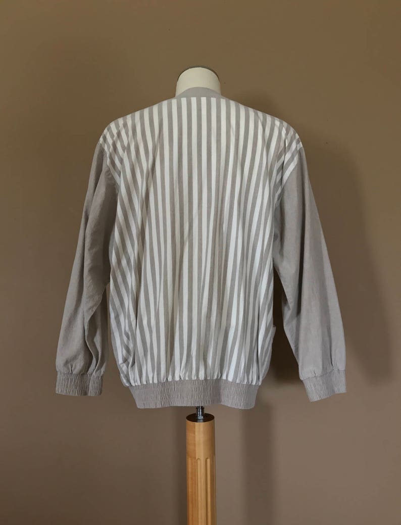 May include: A beige striped long-sleeve shirt with a ribbed hem and cuffs. The shirt is made of a soft, lightweight fabric and has a relaxed fit.