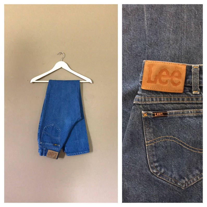 May include: A pair of blue denim jeans with a brown leather Lee label on the back pocket. The jeans are hanging on a white hanger.