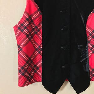 May include: A black velvet vest with a red and black plaid pattern on the sides. The vest has a pointed collar and four buttons down the front.