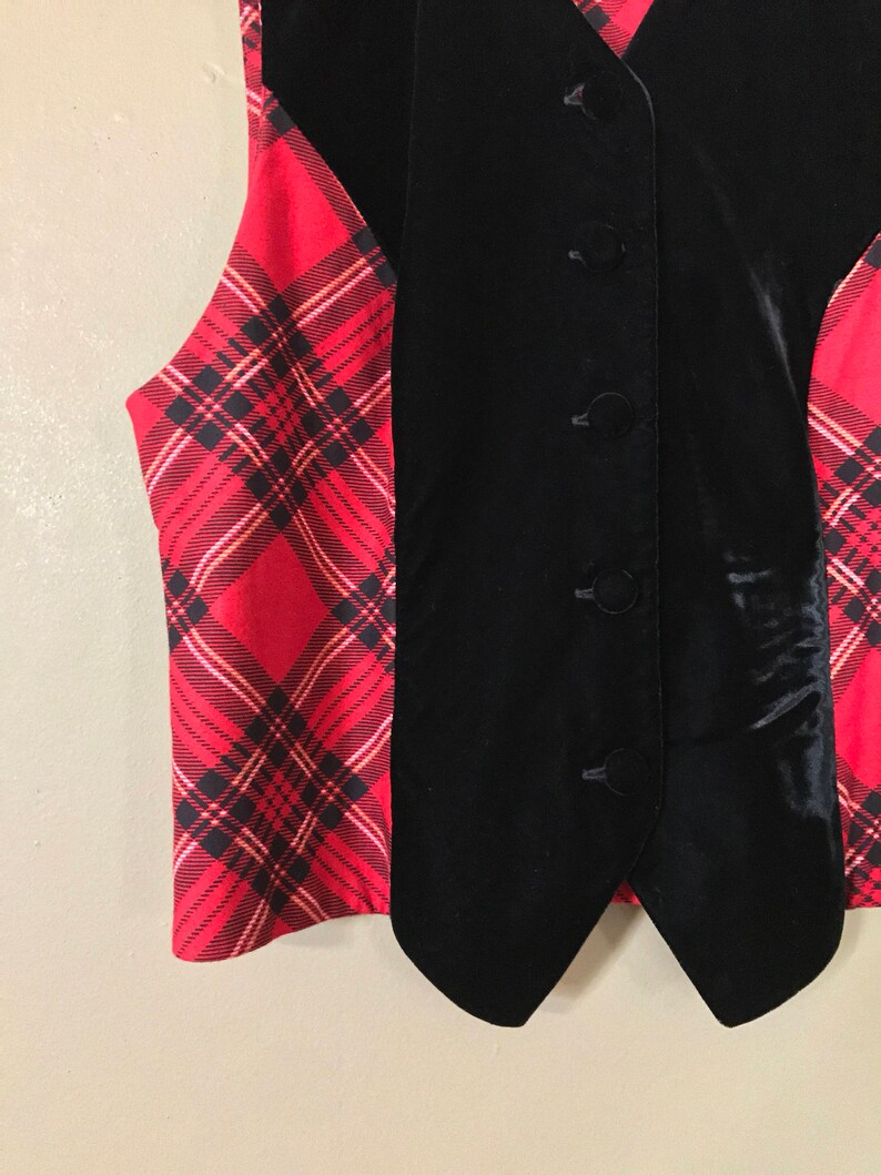 May include: A black velvet vest with a red and black plaid pattern on the sides. The vest has a pointed collar and four buttons down the front.