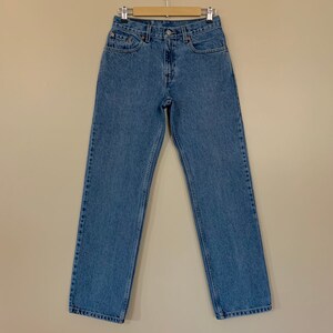 May include: Light blue denim jeans hanging on a wooden hanger. The jeans have a classic five-pocket design, a button and zip closure, and a straight leg fit. The jeans are made of a durable denim fabric.