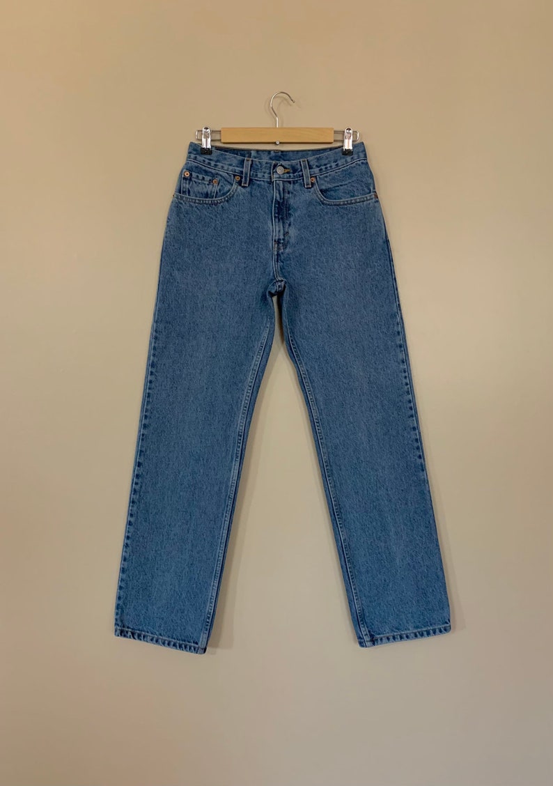 May include: Light blue denim jeans hanging on a wooden hanger. The jeans have a classic five-pocket design, a button and zip closure, and a straight leg fit. The jeans are made of a durable denim fabric.