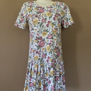 K&ouml;nnte beinhalten: Ein wei&szlig;es Kleid mit einem Blumendruck mit roten, gelben und gr&uuml;nen Blumen. Das Kleid hat kurze &Auml;rmel und einen gerafften Rock.