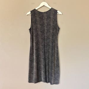 Pu&ograve; includere: Un abito midi senza maniche con motivo bianco e nero appeso a un appendiabiti bianco contro un muro beige.