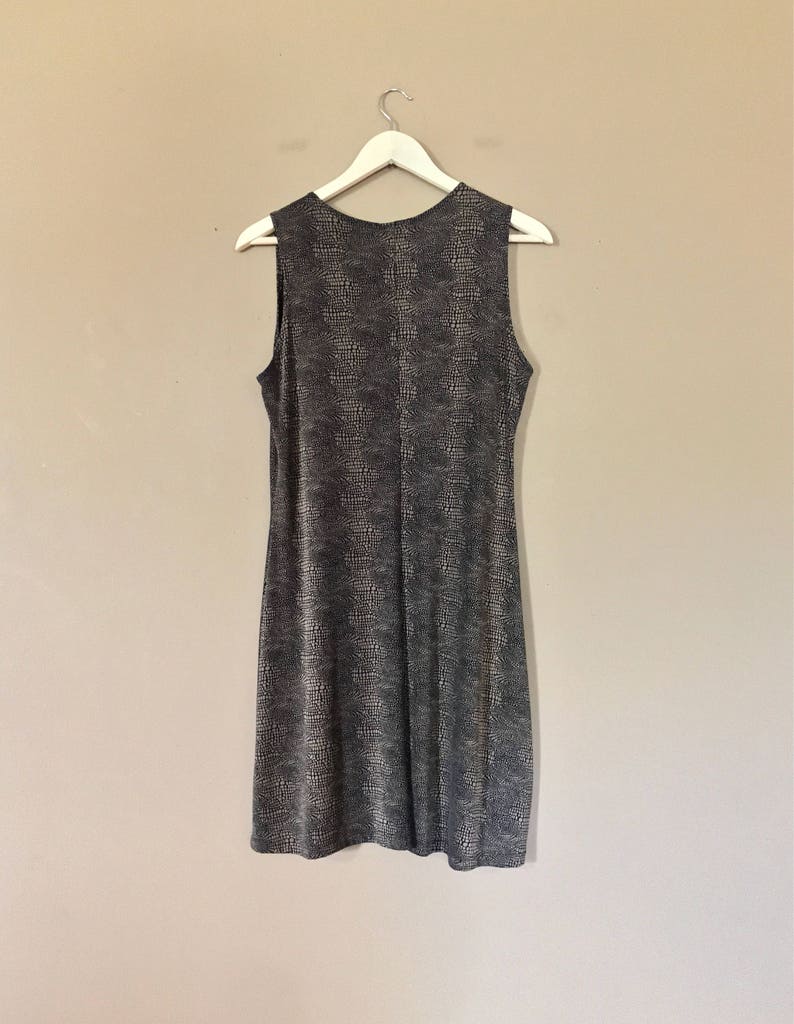 Pu&ograve; includere: Un abito midi senza maniche con motivo bianco e nero appeso a un appendiabiti bianco contro un muro beige.