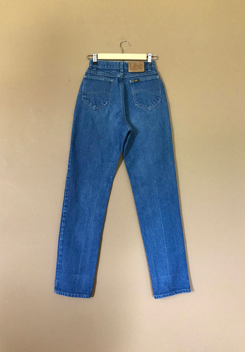 May include: A pair of blue denim jeans with a brown leather Lee label on the back pocket.