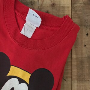 May include: Red t-shirt with a large Mickey Mouse graphic. The shirt has a crew neck and is made of 100% cotton. The tag says "Disney".