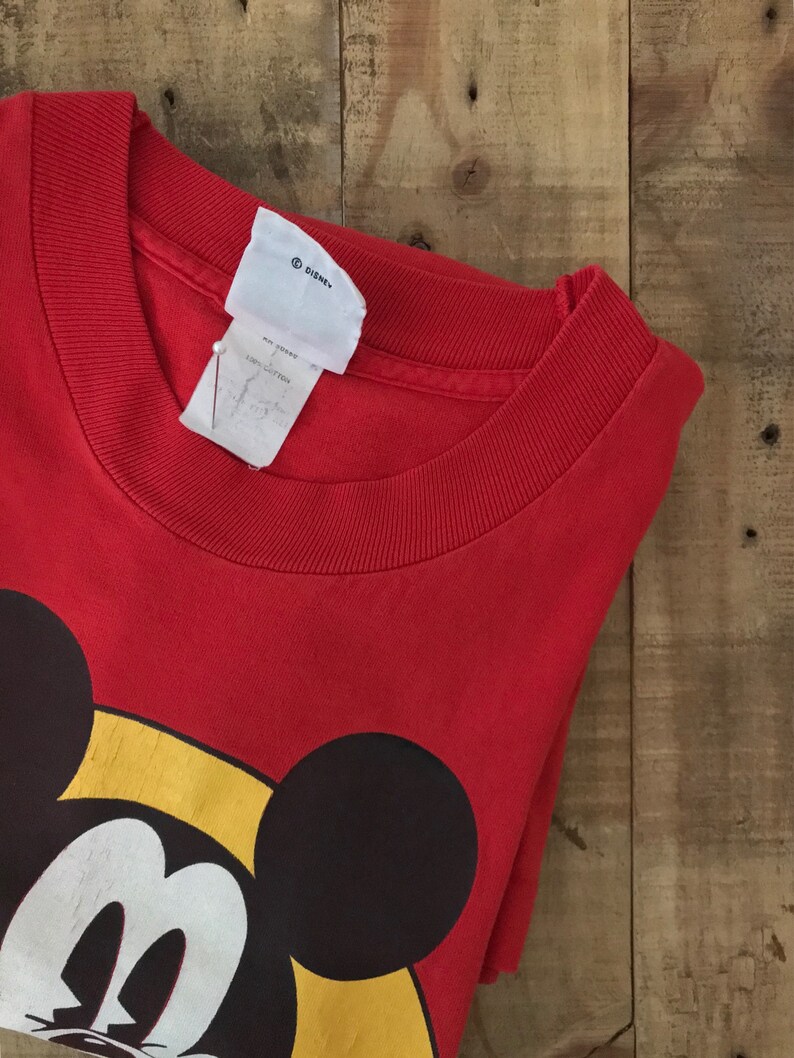 May include: Red t-shirt with a large Mickey Mouse graphic. The shirt has a crew neck and is made of 100% cotton. The tag says "Disney".