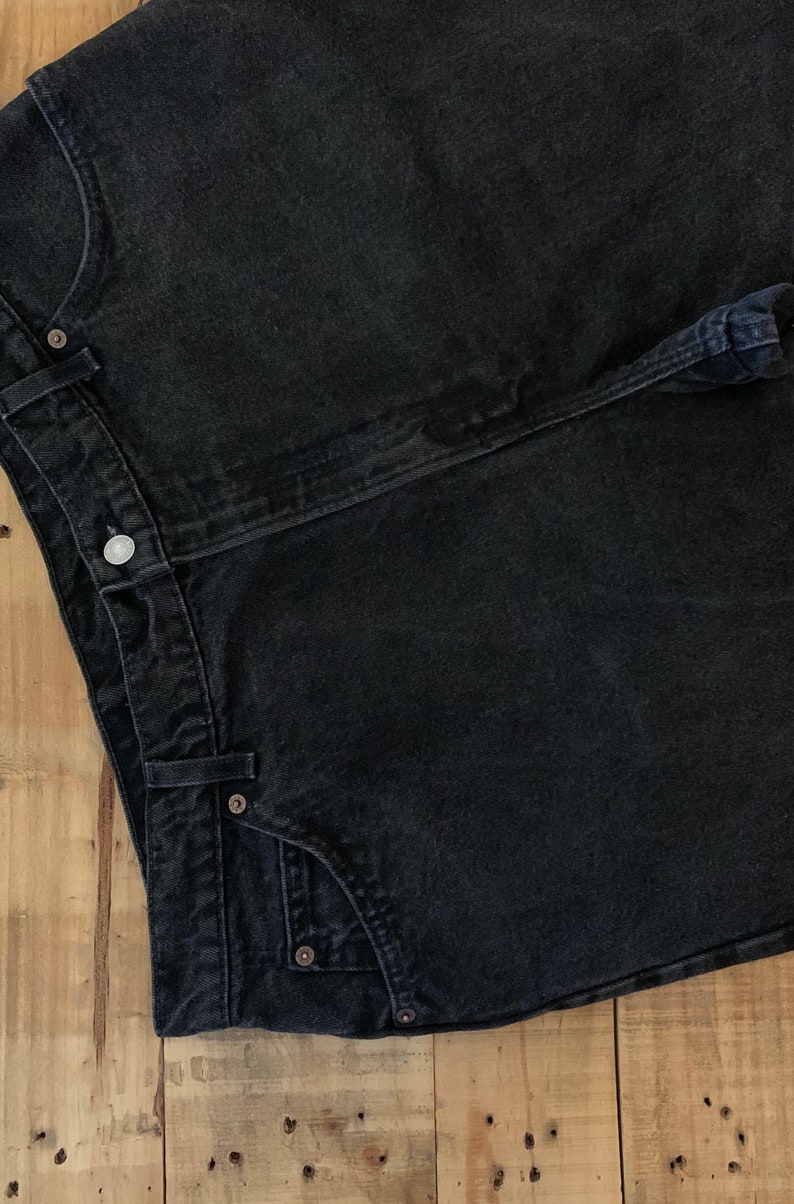 May include: A pair of black denim jeans with a button fly and a single back pocket.