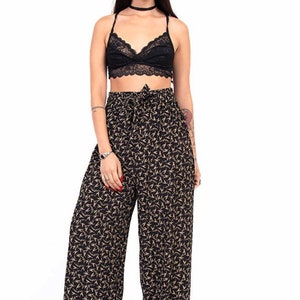Puede incluir: Una mujer con un bralette de encaje negro y pantalones anchos con estampado floral negro y dorado. Tambi&eacute;n lleva un sombrero negro y zapatos negros.