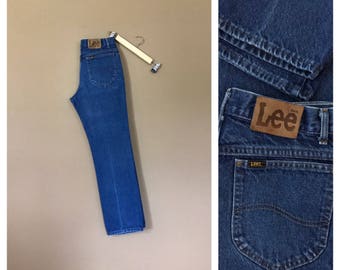 May include: A pair of blue denim jeans with a brown leather Lee label on the back pocket. The jeans have a straight leg and a classic fit.