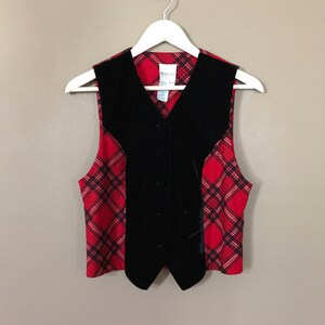 May include: A black velvet vest with a red and black plaid pattern on the sides. The vest has a button closure and a V-neck.
