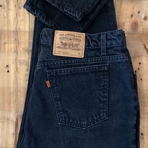 May include: A pair of black Levi Strauss & Co. jeans with a brown leather patch and a small size tag. The jeans are folded in half and have a back pocket.