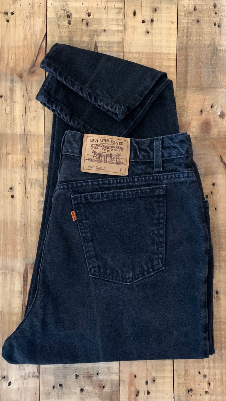 May include: A pair of black Levi Strauss & Co. jeans with a brown leather patch and a small size tag. The jeans are folded in half and have a back pocket.