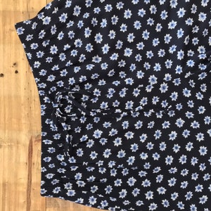Puede incluir: Una falda azul marino con estampado floral blanco. La falda tiene una cintura con cord&oacute;n.