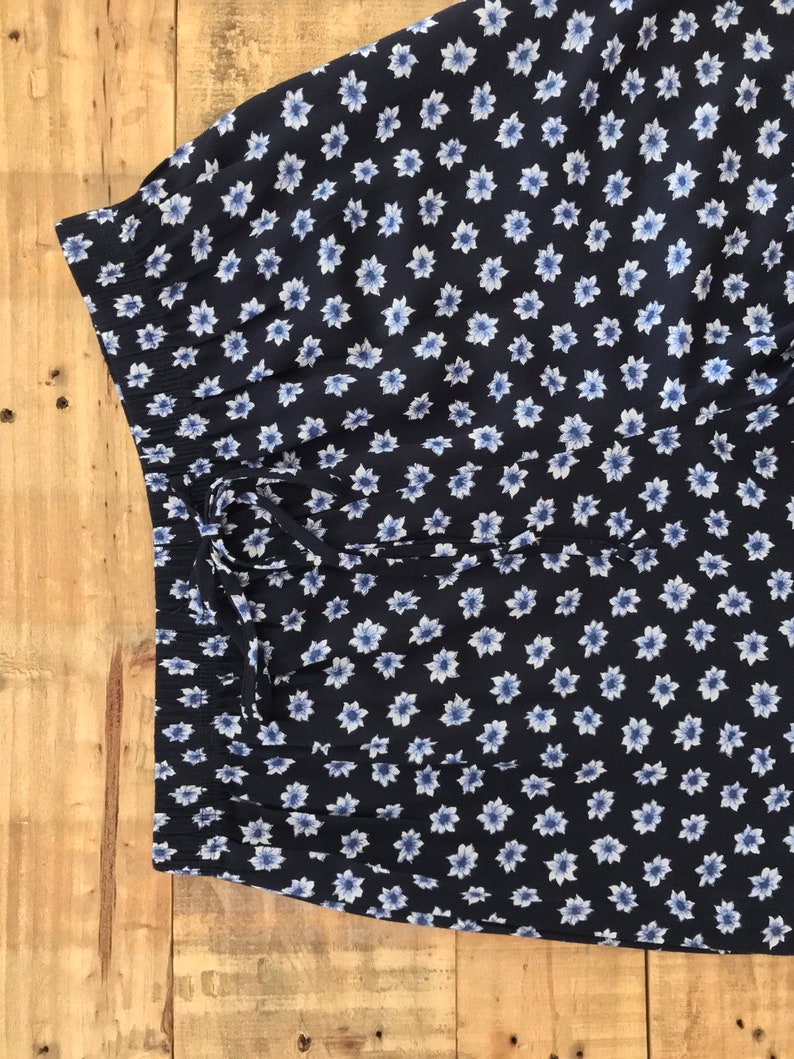 Puede incluir: Una falda azul marino con estampado floral blanco. La falda tiene una cintura con cord&oacute;n.
